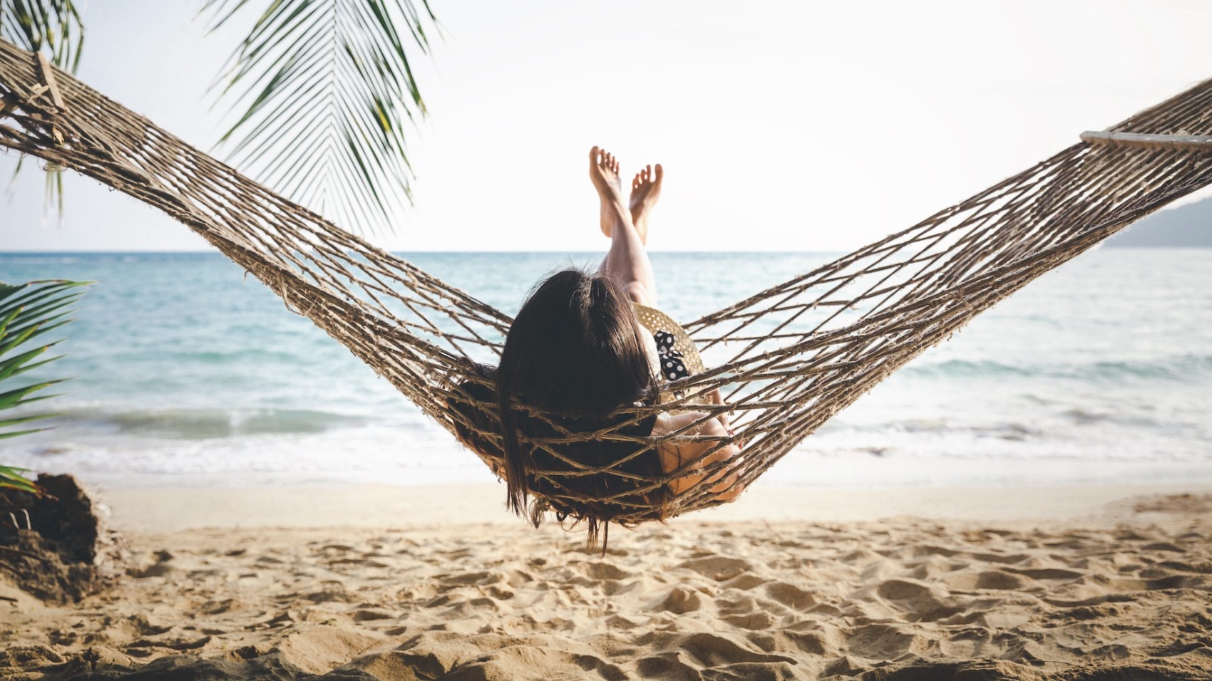 Summer vacations concept, Happy woman with white bikini, hat and shorts Jeans relaxing in hammock on tropical beach at sunset, Koh mak, Thailand