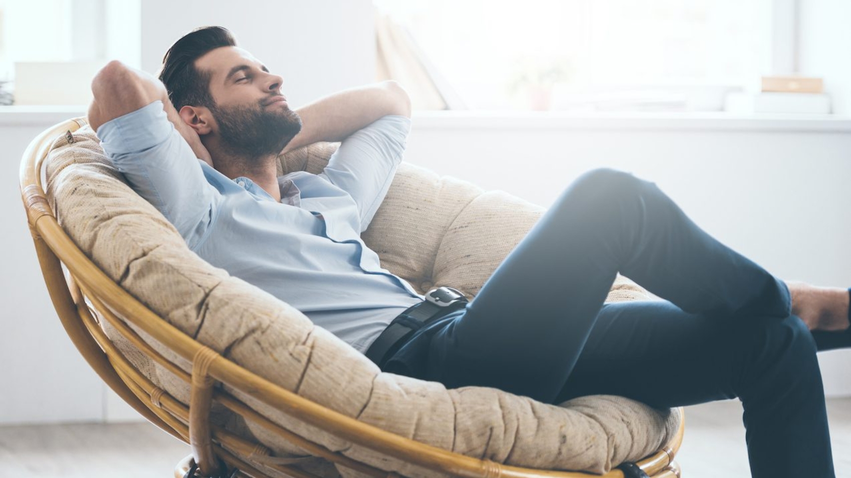 Total relaxation. Handsome young man keeping eyes closed and holding hands behind head while sitting in big comfortable chair at home