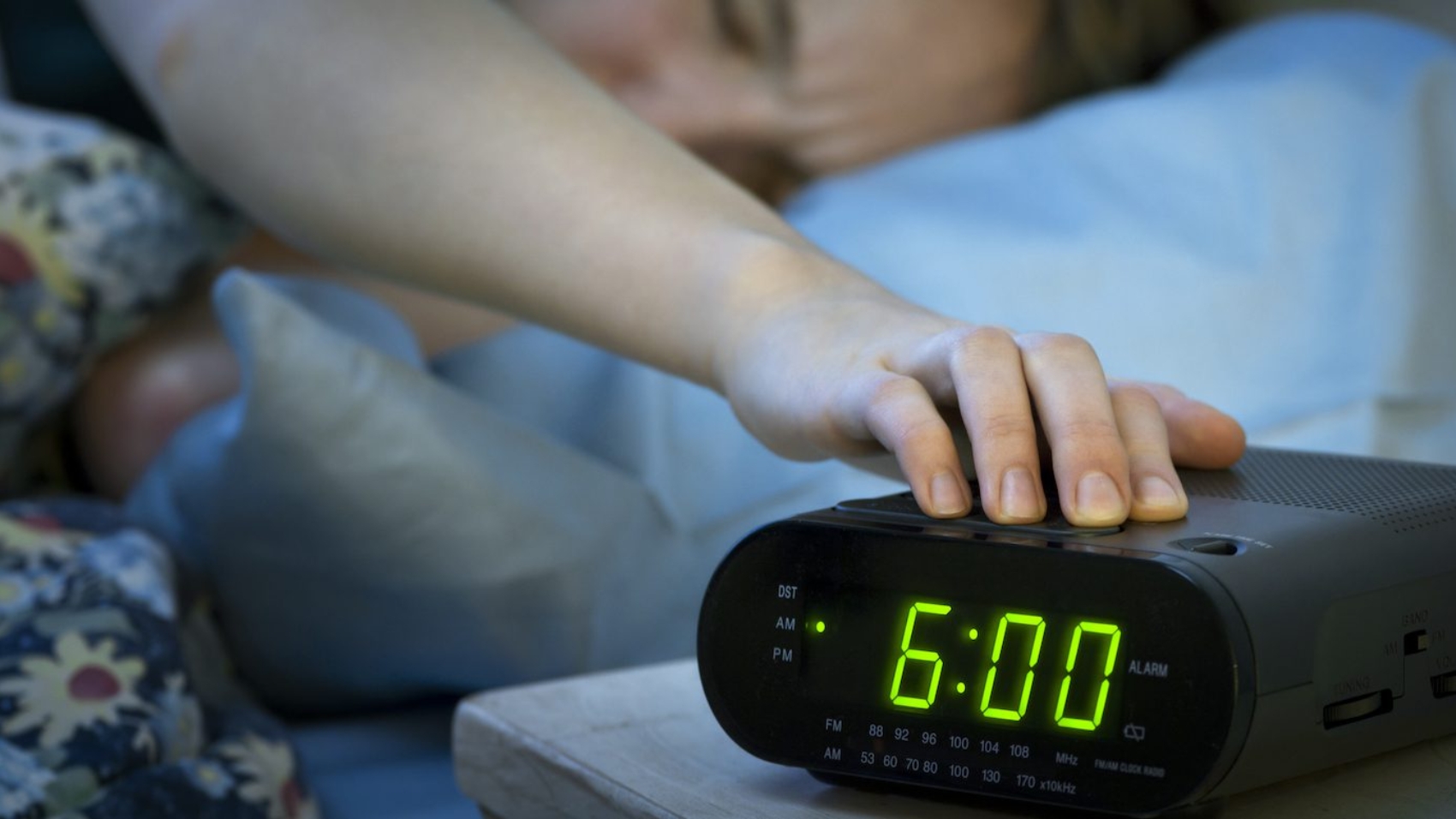 Young woman pressing snooze button on early morning digital alarm clock radio