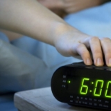 Young woman pressing snooze button on early morning digital alarm clock radio