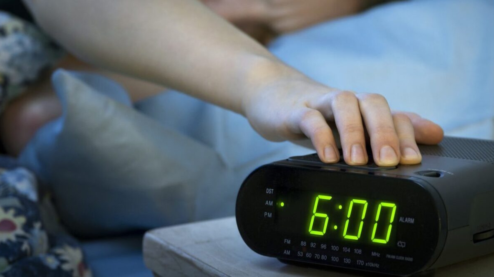 Young woman pressing snooze button on early morning digital alarm clock radio