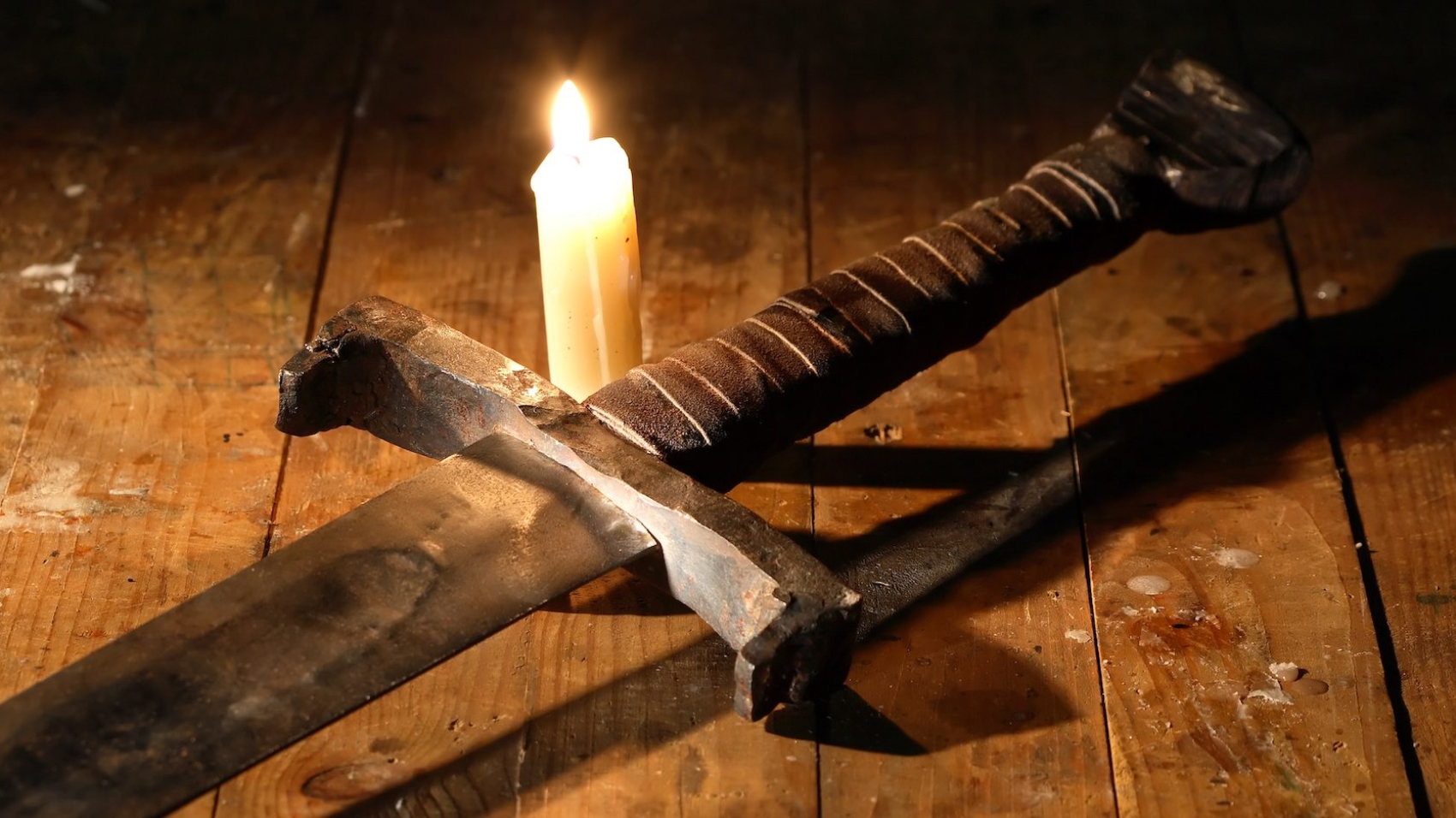 Vintage still-life with ancient sword near lighting candle on wooden board