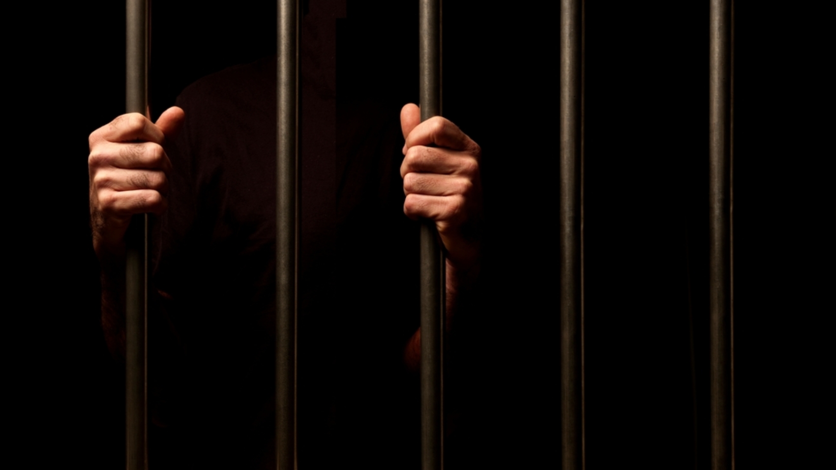 Hands,Of,A,Prisoner,Behind,Prison,Bars,On,Black,Background