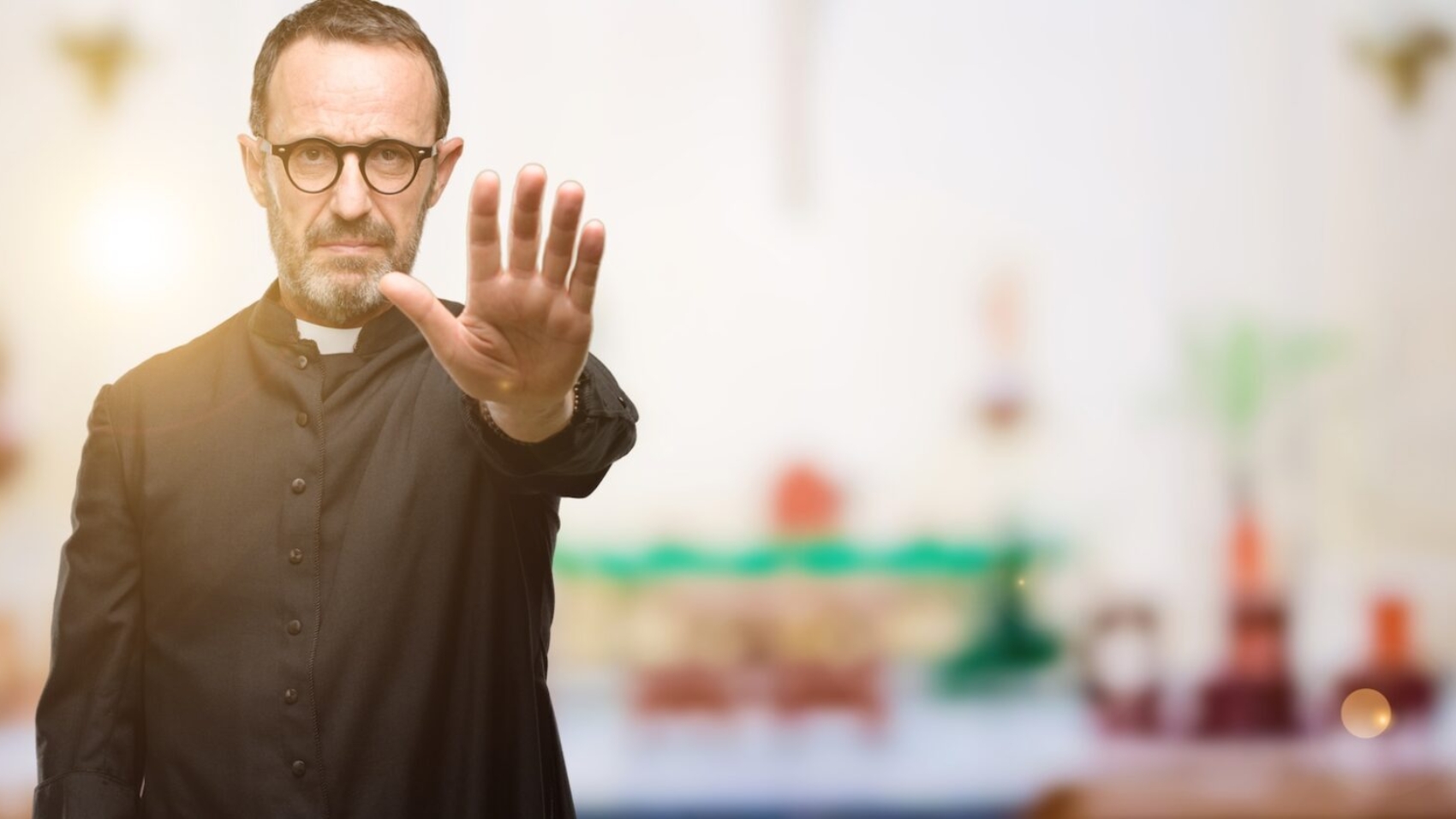 Priest religion man annoyed with bad attitude making stop sign with hand, saying no, expressing security, defense or restriction, maybe pushing at church